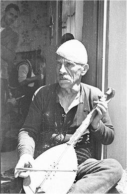 Black and white photo of a seated old man with a hat and a gusle (a stringed instrument) Black and white photo of a seated old man with a hat and a gusle (a stringed instrument)