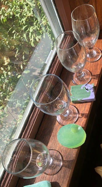 A group of wine glasses on a window sill

Description automatically generated