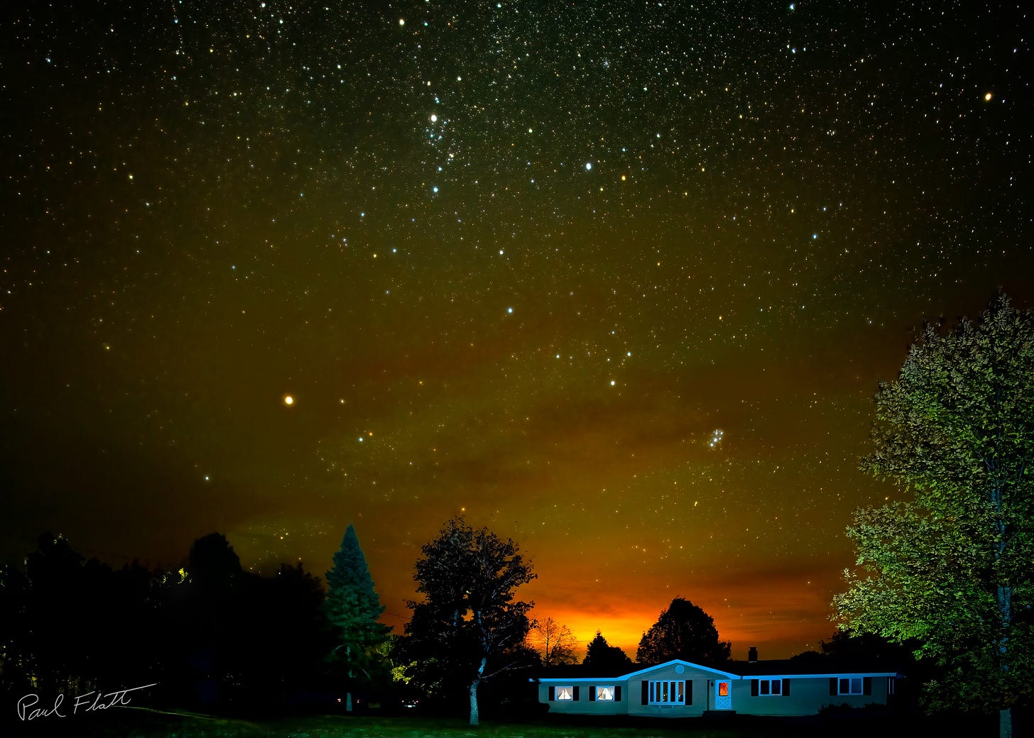 House with stars and sky glow from nearby city.