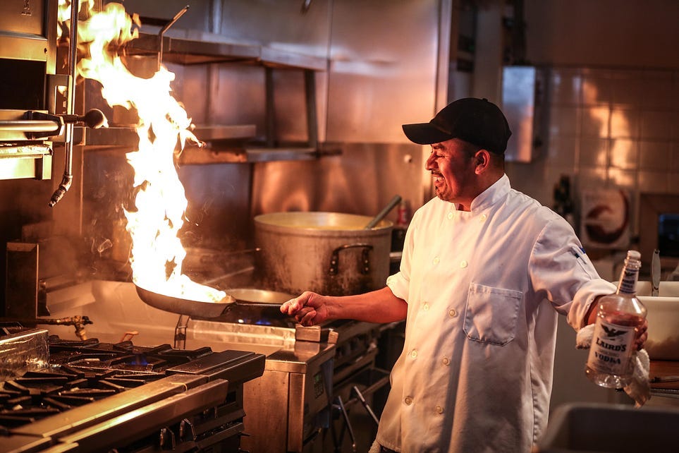 Picture of a chef with a flaming pan over the burner
