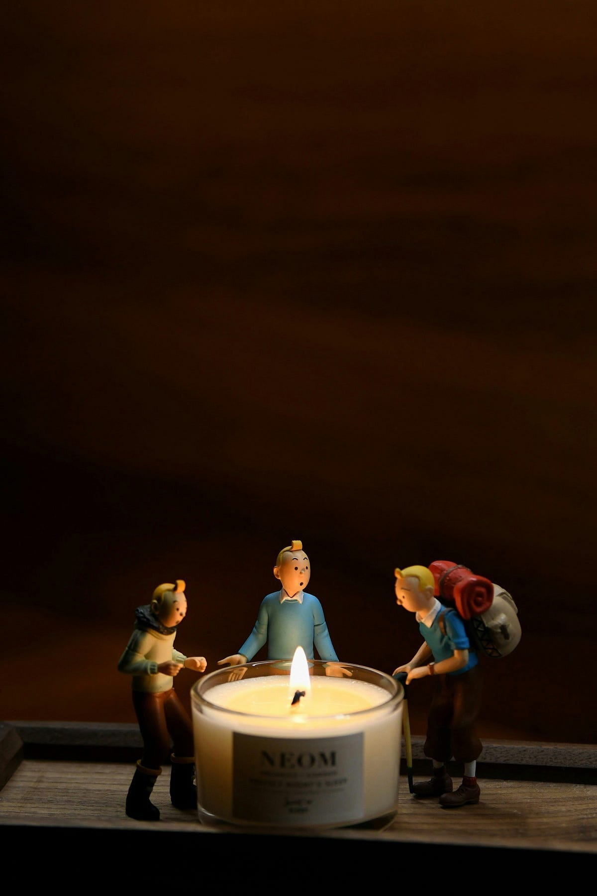 3 childlike hiker figurines standing around a lit candle 3 childlike hiker figurines standing around a lit candle
