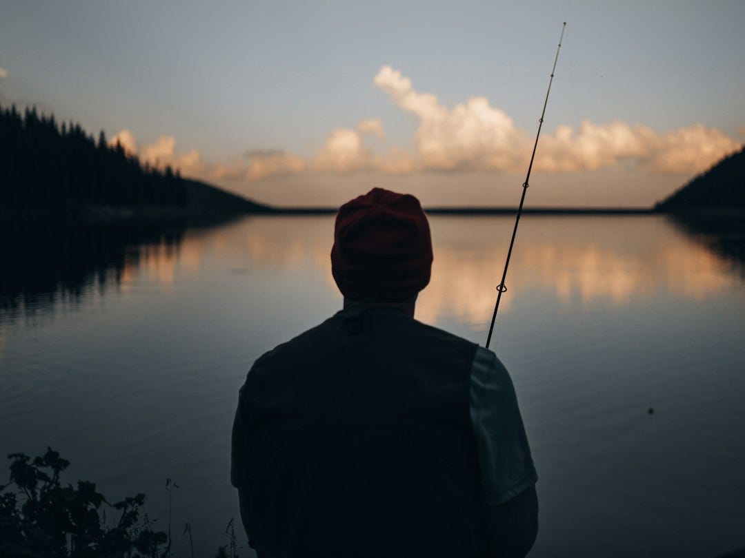 man in black jacket and black knit cap standing near lake during daytime