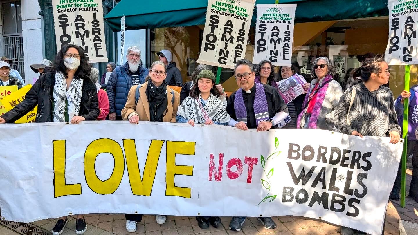 Bruce, his wife, and their daughters at a street protest carrying a banner that reads "LOVE not Borders-Walls-Bombs"