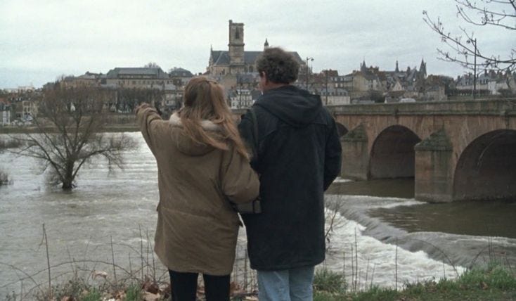 This may contain: a man and woman standing next to each other looking at the water in front of them