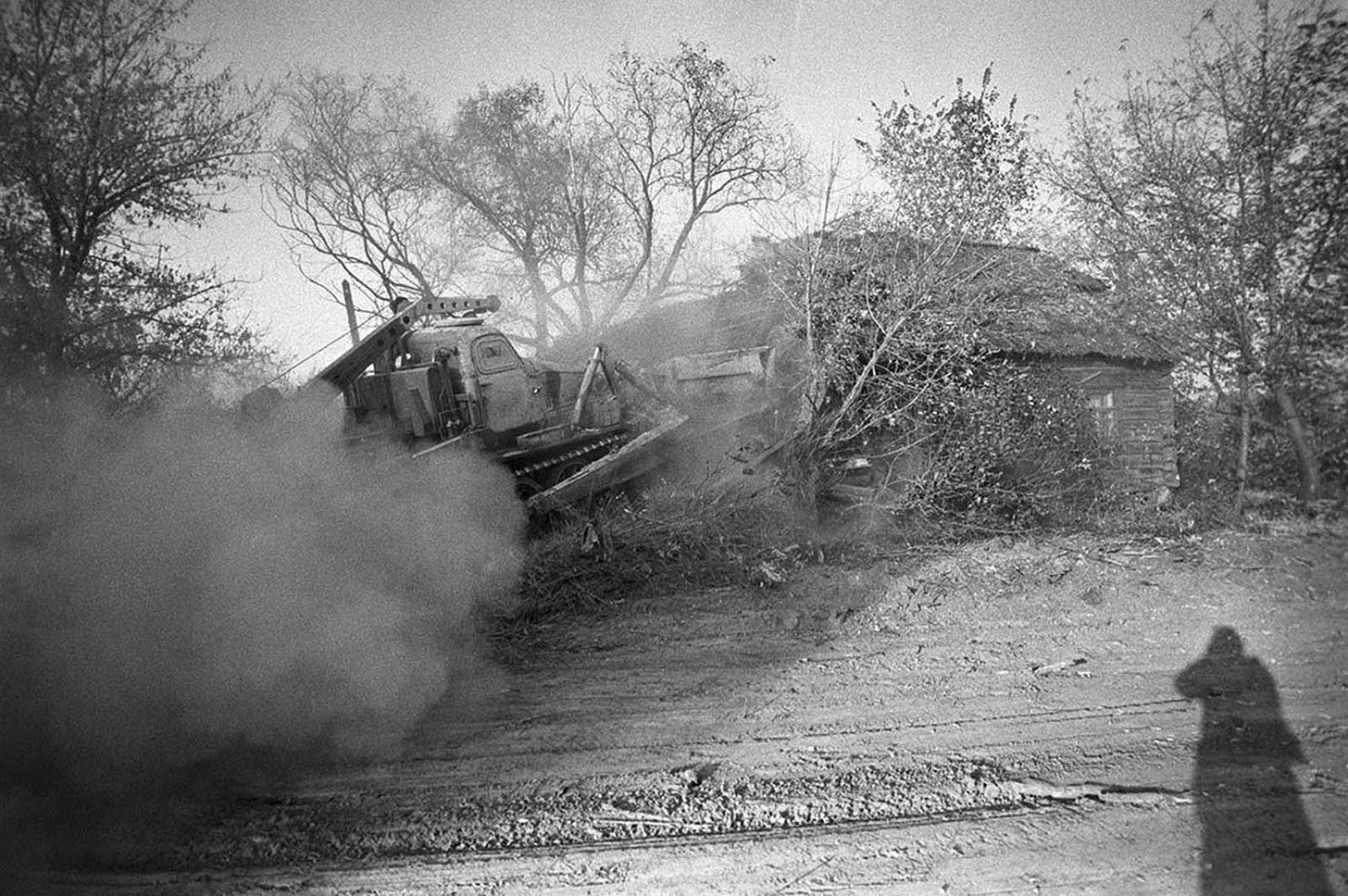 A bulldozer buries a contaminated house, illustrating the grim fate of entire villages entombed after the Chernobyl disaster.