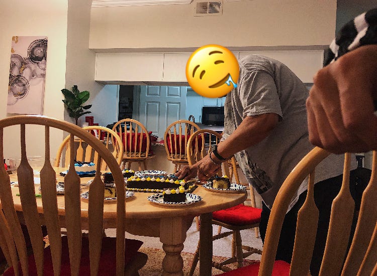Man hovered over a chocolate frosting covered birthday cake cutting slices onto paper plates in the dinning room.