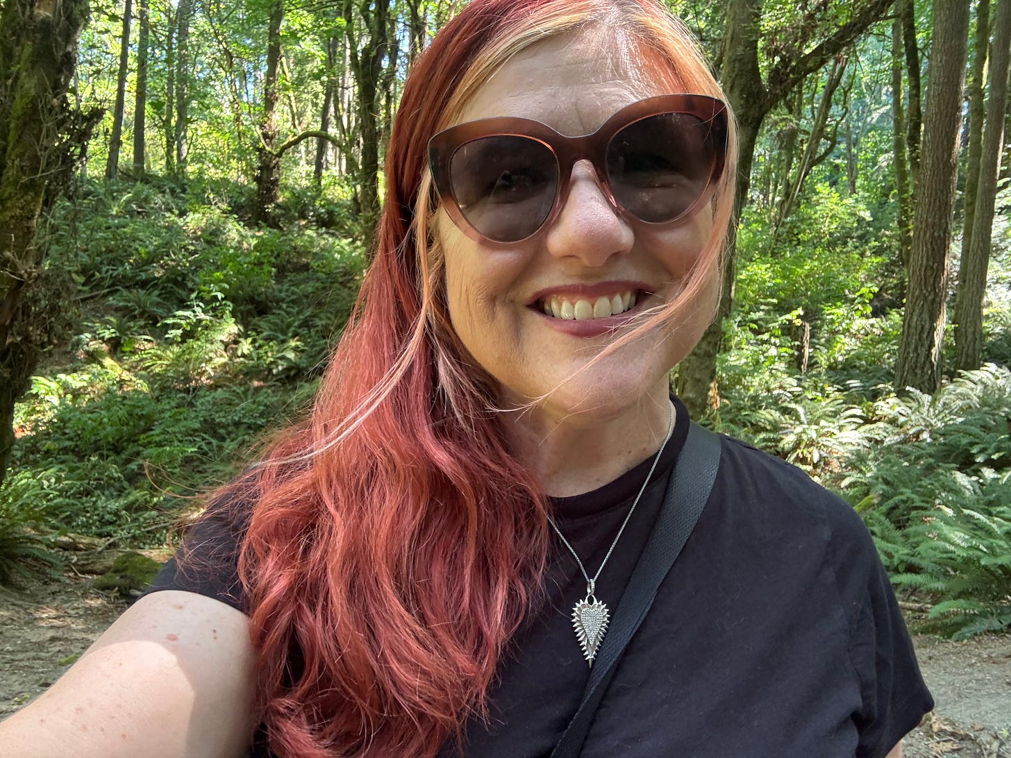 Red-haired woman in the woods with sunglasses and a black t-shirt.