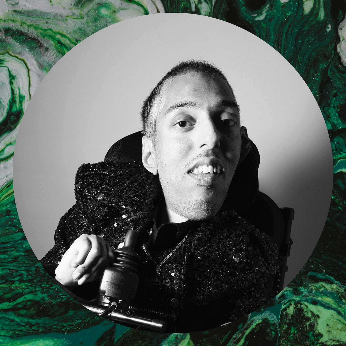 Image Description: Sexy, spicy, and sacred. On a green fluid abstract painting background, there’s a Black and white photo of Sulaiman (a wholeheartedly Disabled AF, British-Pakistani man with buzzcut black hair) by the legendary photographer Rankin and his team at the Art Car Boot Fair in London from September 2023. Sulaiman sits in his new black and green power wheelchair since walking and standing are SO overrated, as Sulaiman says. The last photo is with Rankin. He is wearing his pure silver chain and pendant that his late Nanaji (maternal grandfather) made for Sulaiman when he was 15 over 23 years ago and that Sulaiman rediscovered early this year. The silver pendant says “Raja Sulaiman” in Urdu, as that’s what Sulaiman’s Nanaji used to call him. Sulaiman wears this pendant to remember and honour his late Nanaji, his ancestors, and his descendants because Sulaiman understands (and respects) that he is the link from his ancestors to his descendants. And yes, he knows his pendant is facing backwards, but it’s deliberate and facing his heart. Sulaiman is also wearing his black sequin biker jacket via @phixclothing.  Sulaiman smiles while feeling joyful and badass in his radically bold, wild, fearless existence. Also, although the description is of the colour look, the photo is black and white. End.