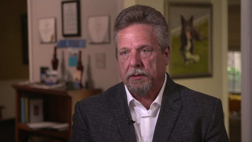 MCU of former Boeing Quality Manager John Barnett sitting in his house wearing a white open collared shirt and grey jacket