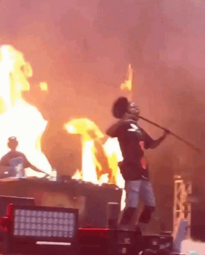 a man is standing on a stage holding a stick in front of a fire a man is standing on a stage holding a stick in front of a fire
