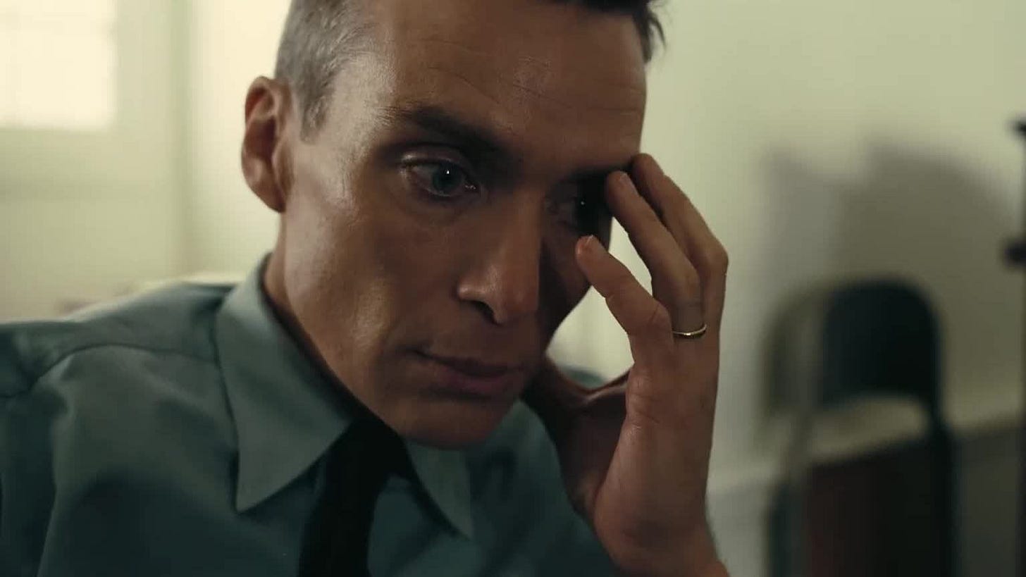 Movie still from Oppenheimer. Oppenheimer holds a hand to his face, distraught.