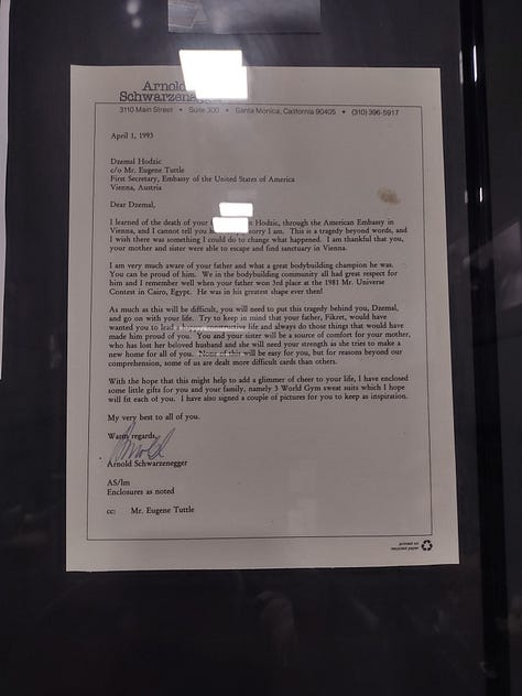 The top left image shows a letter from Arnold Schwarzenegger to the zon of Yugoslavian bodybuilding champion, Fikret Hodzic. The top middle image shows the gramed letter together with a picture of Schwarzenegger . The top right image shows a bodybuilding shirt from Schwarzenegger in yellow that says "World Gym." The bottom left image shows the text describing Fikret Hodzic's life and death. The bottom right image shows a gold medal won by Fikret Hodzic at the European Bodybuilding Championships.