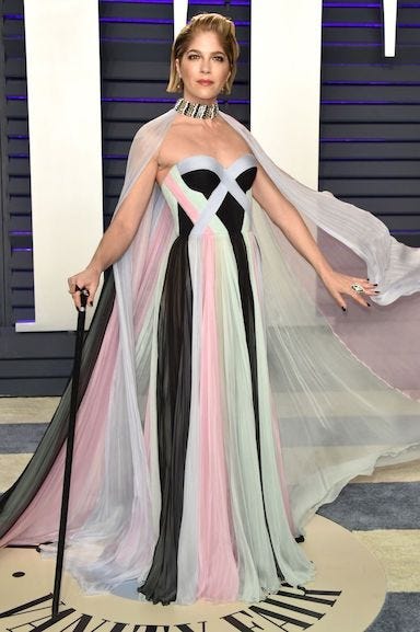 Selma Blair at the 2019 Vanity Fair Oscars Party. Full body picture, she’s wearing multicolored gown with a sheer cape. She stands with her arms open, cane in right hand. Selma Blair at the 2019 Vanity Fair Oscars Party. Full body picture, she’s wearing multicolored gown with a sheer cape. She stands with her arms open, cane in right hand.