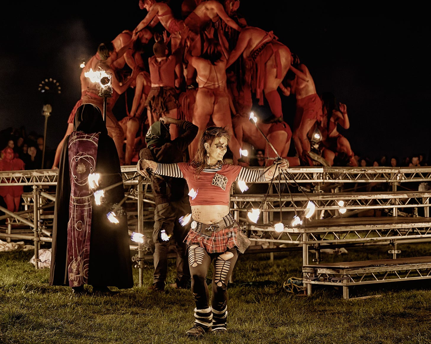 This documentary fieldwork photograph shows a member of the team Firearchy juggling with the Circle of Red team, who are in playful embrace after the Summer Green Man has been crowned. Beltane, Edinburgh 2026