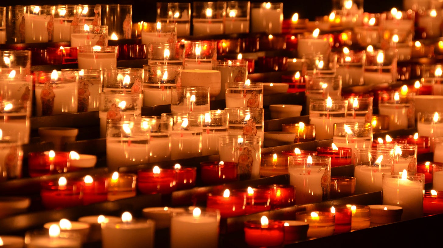 Row after row of small votive candles in white and red. They burn, pushing away the darkness.