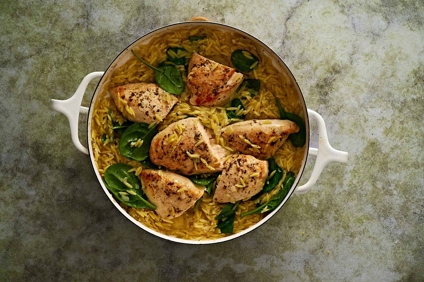 Lemon chicken orzo pasta served in a pot with fresh spinach and juicy seared chicken breasts.