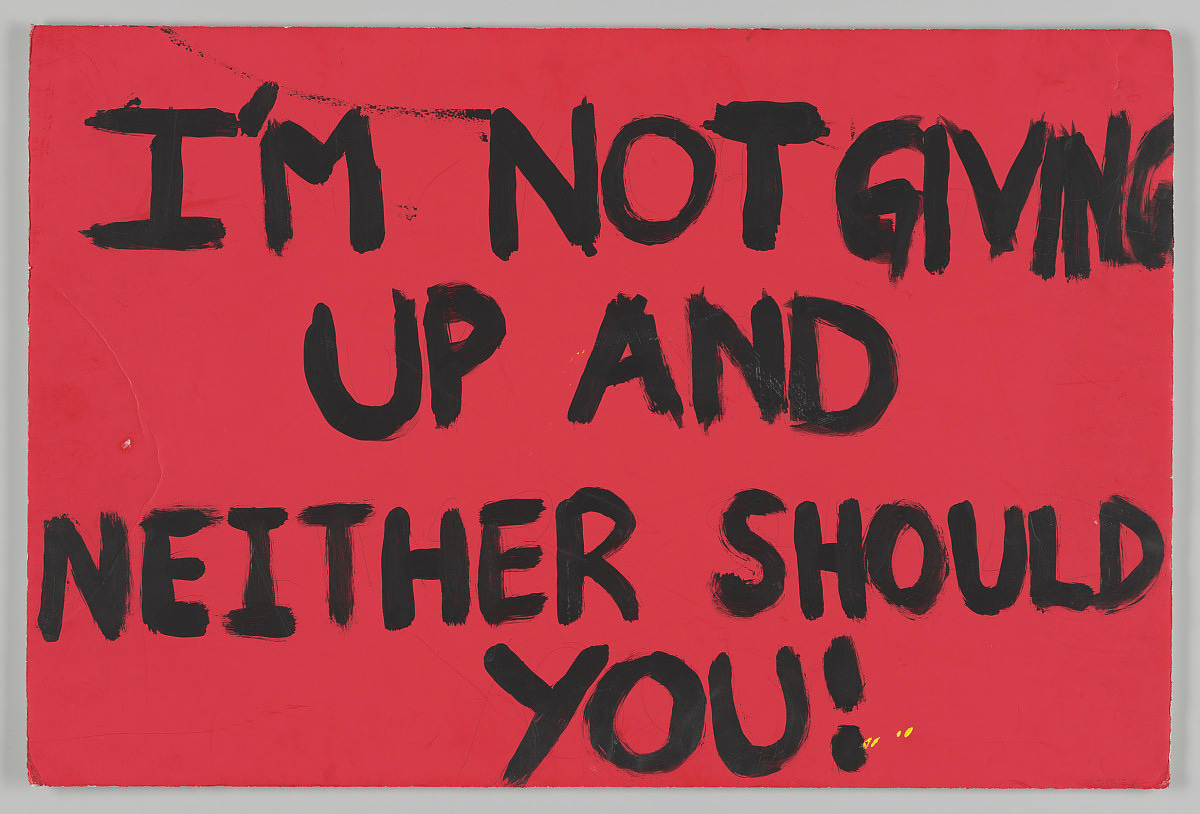 Handwritten poster from the 2017 Women’s March on Washington. Red background with black hand-painted text [I’M NOT GIVING / UP AND / NEITHER SHOULD YOU!].