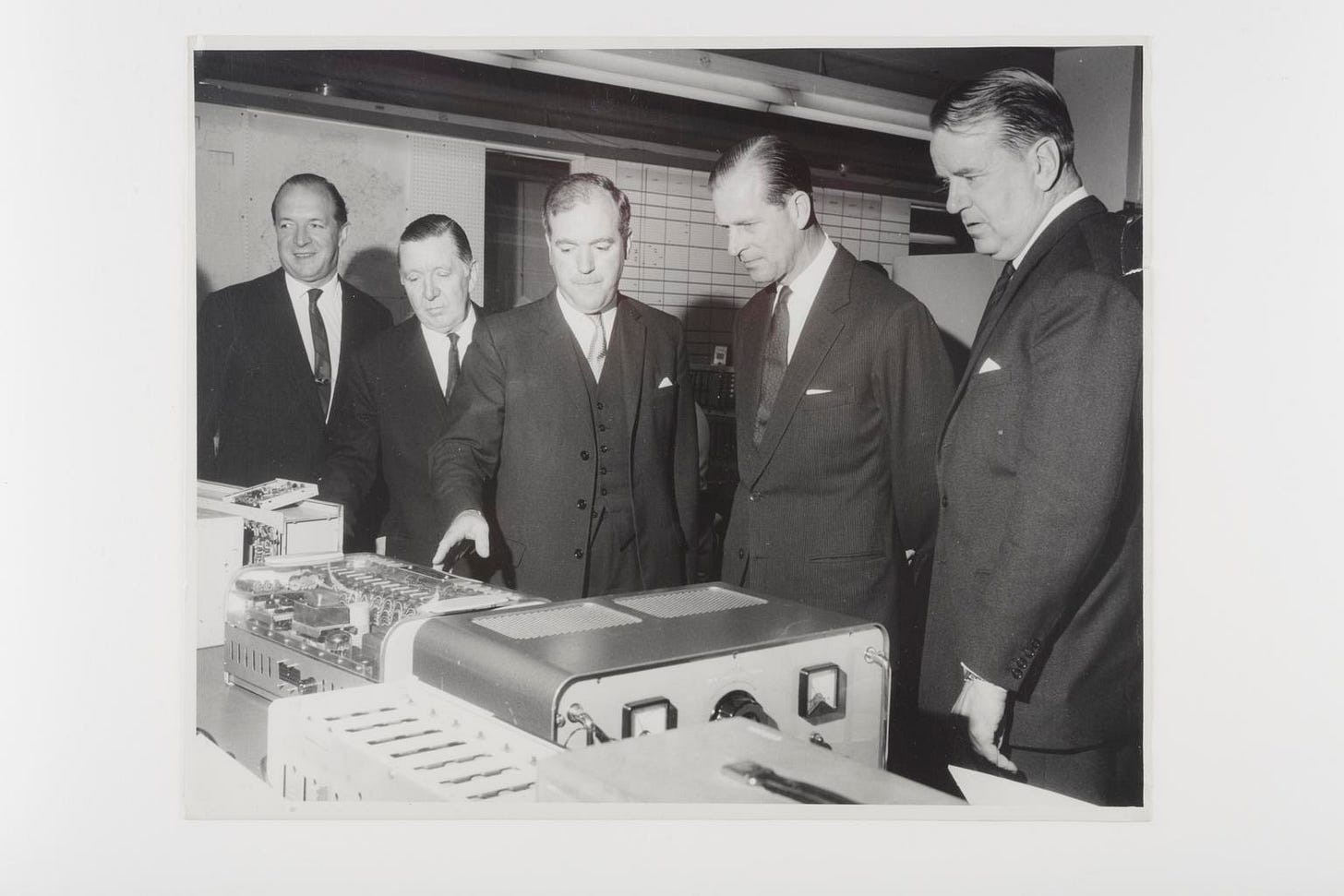Image of HRH Duke of Edinburgh being shown some complex equipment - presumably on a factory tour.