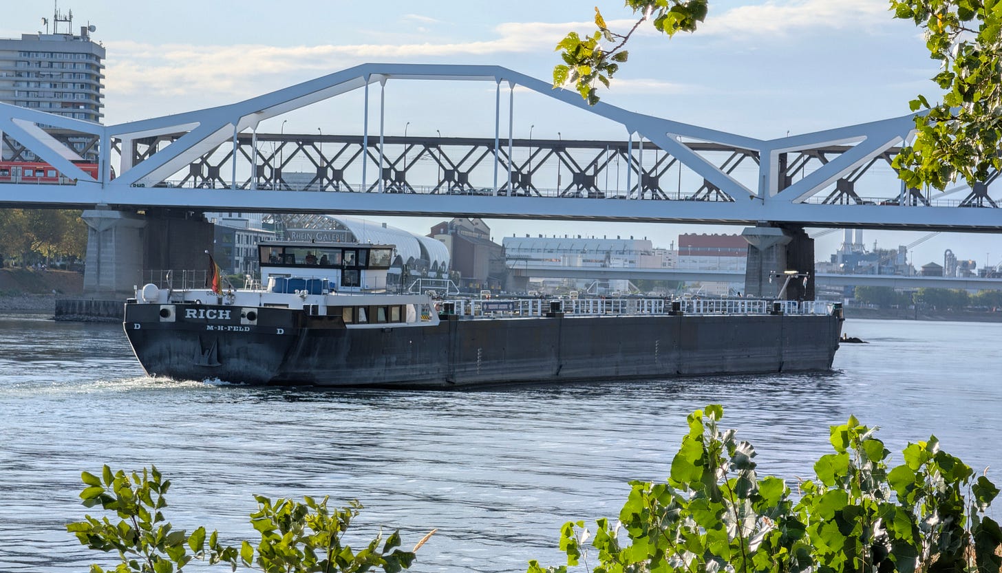 Inland cargo barge on the Rhine at Ludwigshafen with Rhein Galerie and a road bridge in the background, August 2026 Inland cargo barge on the Rhine at Ludwigshafen with Rhein Galerie and a road bridge in the background, August 2026