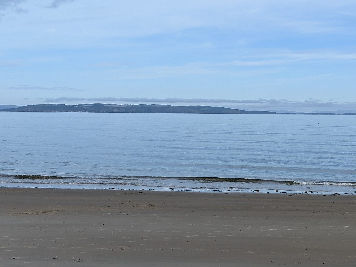 Beach with a calm flat blue sea at Nairn stretching out to the Black isle hills beyond