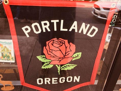Portland Rose banner, Mt Hood, man wearing a hat, sunglasses, and blue shirt by the water