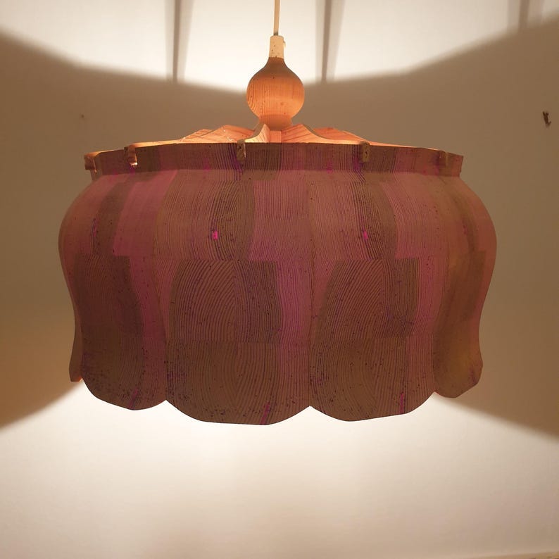 May include: A hanging pendant light fixture with a scalloped shade. The shade is a mix of brown and pink tones, with a textured, layered design. The light fixture is suspended from a white cord and has a wooden top. May include: A hanging pendant light fixture with a scalloped shade. The shade is a mix of brown and pink tones, with a textured, layered design. The light fixture is suspended from a white cord and has a wooden top.