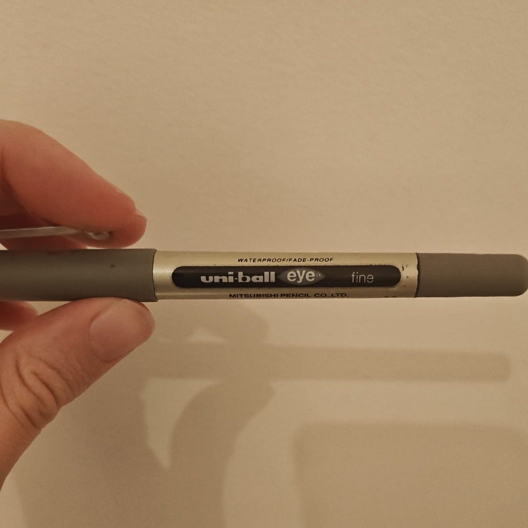 Grey Uni-ball Eye fine pen held in front of a plain wall, photographed as part of Elspeth Wilson’s Tarot DMs interview.