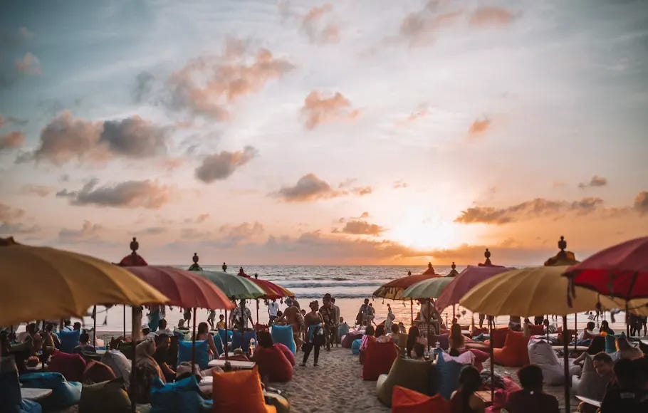 A vibrant photograph of a beach in Southeast Asia, with colorful umbrellas and bean bags, as international tourists enjoy the sunset. The scene depicts the rapid post-pandemic recovery in tourism in the region, bringing with it concerns about overtourism. A vibrant photograph of a beach in Southeast Asia, with colorful umbrellas and bean bags, as international tourists enjoy the sunset. The scene depicts the rapid post-pandemic recovery in tourism in the region, bringing with it concerns about overtourism.