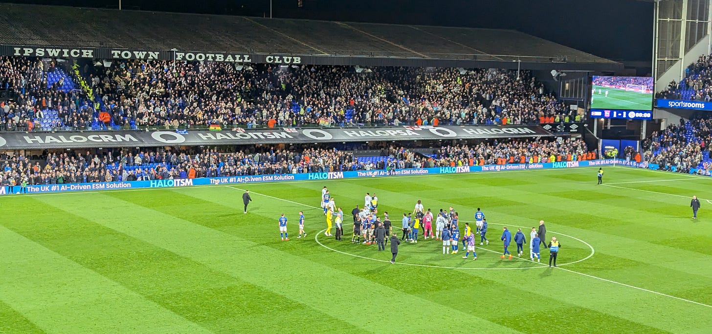 Ipswich players and staff confront referee Tim Robinson in the centre circle after Ipswich 1-1 Leicester