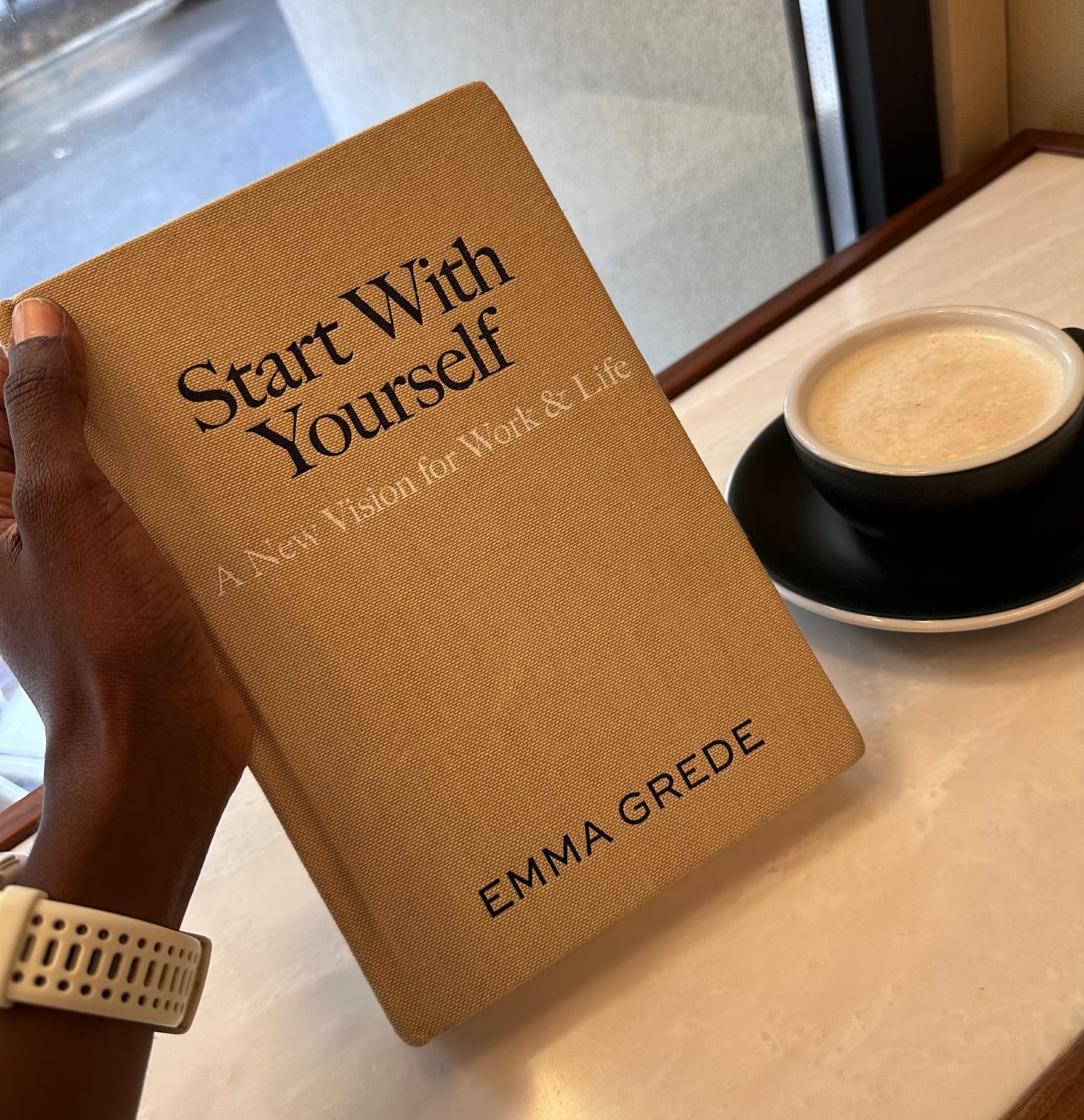 Start with Yourself by Emma Grede, held at a café table next to a chai latte