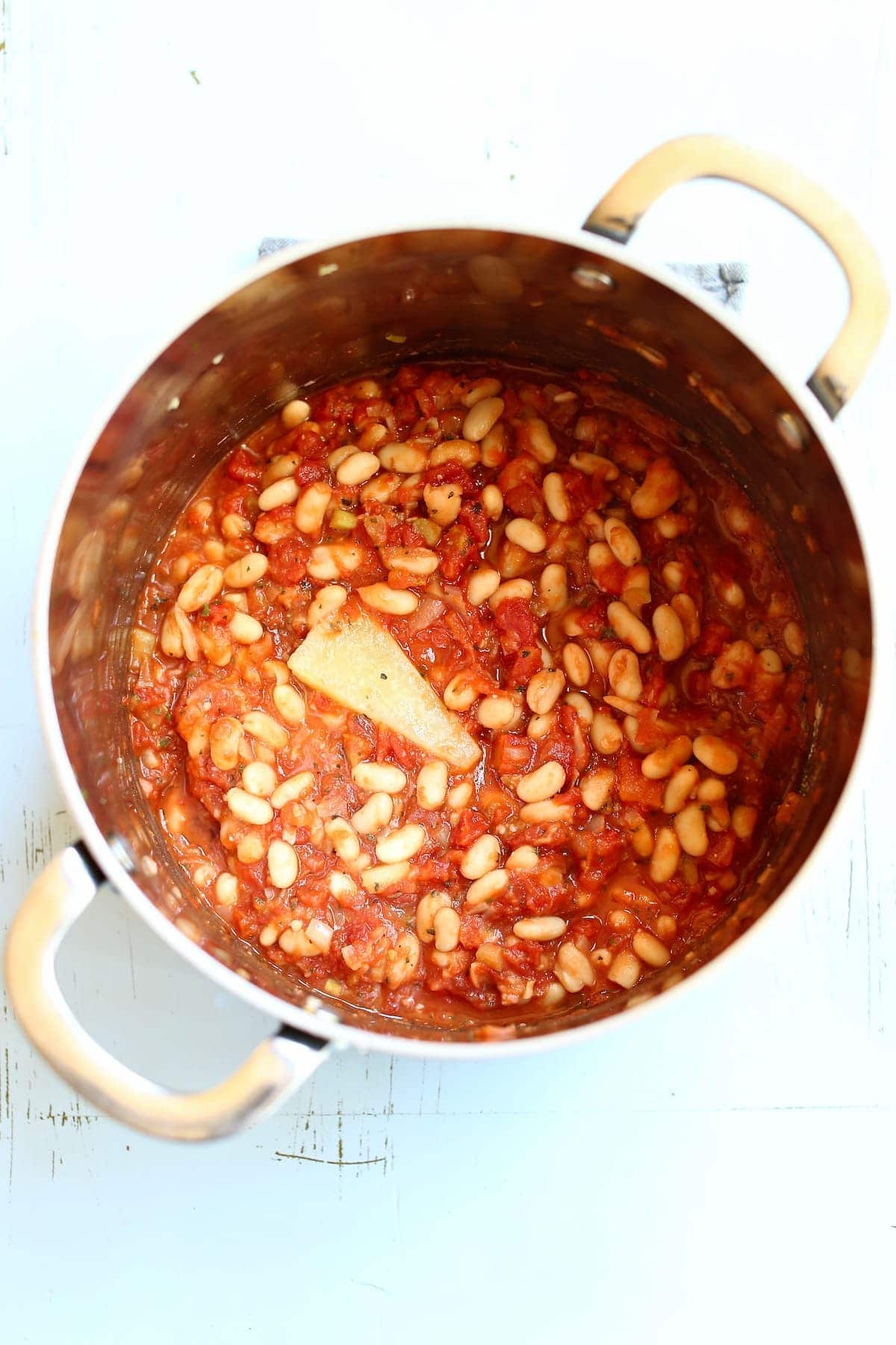 a dutch oven of beans and pasta and a parmesan cheese rind showing a process step in the cooking process.