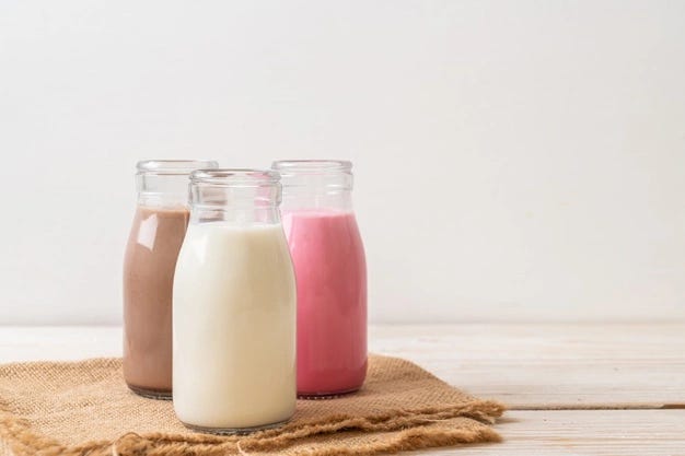 Three glass bottles with chocolate milk, normal white milk, and pink milk.
