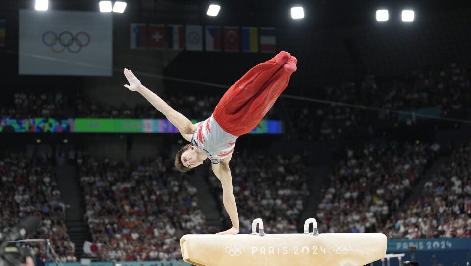 A man with his body in the air diagonally, balancing with one hand on a pommel horse. A man with his body in the air diagonally, balancing with one hand on a pommel horse.