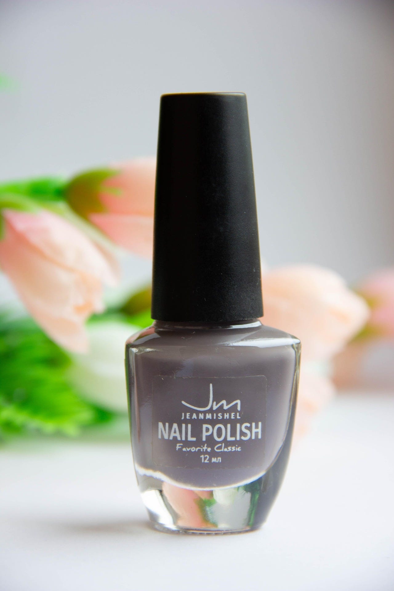 Gray Jeanmishel nail polish bottle labeled ‘Favorite Classic’ 12 ml, standing upright with a black cap against a soft floral background Gray Jeanmishel nail polish bottle labeled ‘Favorite Classic’ 12 ml, standing upright with a black cap against a soft floral background