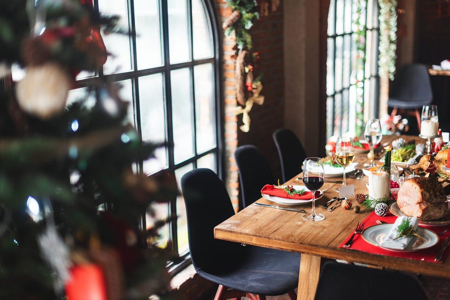 Empty indoor restaurant dining table set for December trading with festive decor and natural window light in the background Empty indoor restaurant dining table set for December trading with festive decor and natural window light in the background