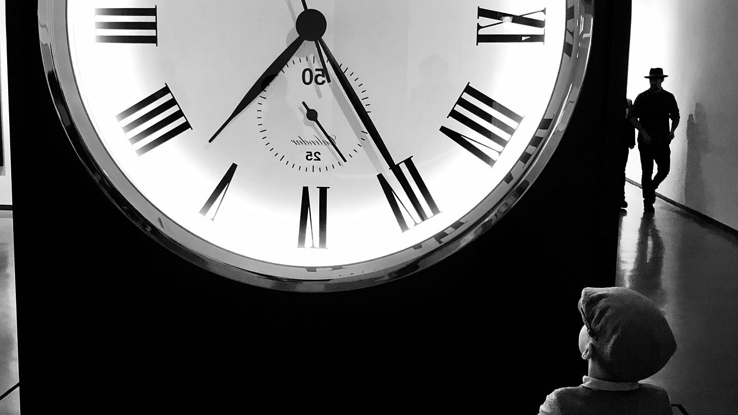 Seen from behind, a young boy looks at a very large standing clock as a man, seen in silhouette, walks towards the viewer from around the side. The image has been left-right reversed so that the Roman-numeral hour designations on the clock's face appear to run backwards.