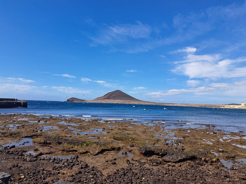 A picture of red mountain protruding from the ocean.