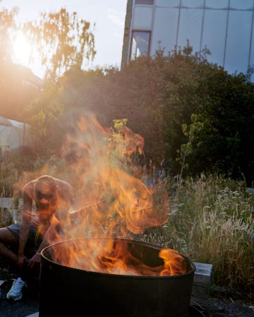 Un jeune homme, assis dans l'hebre, la tête baissée, à côté d'un barbecue d'où s'élève une flamme