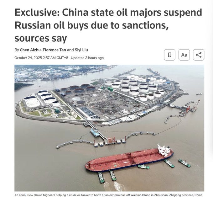 Aerial view of an industrial oil terminal on an island in the Yangtze River in Zhoushan, Zhejiang province, China, featuring multiple large white storage tanks clustered together, surrounded by water, with a red-hulled crude oil tanker ship docked nearby assisted by tugboats, and several docks extending into the river.