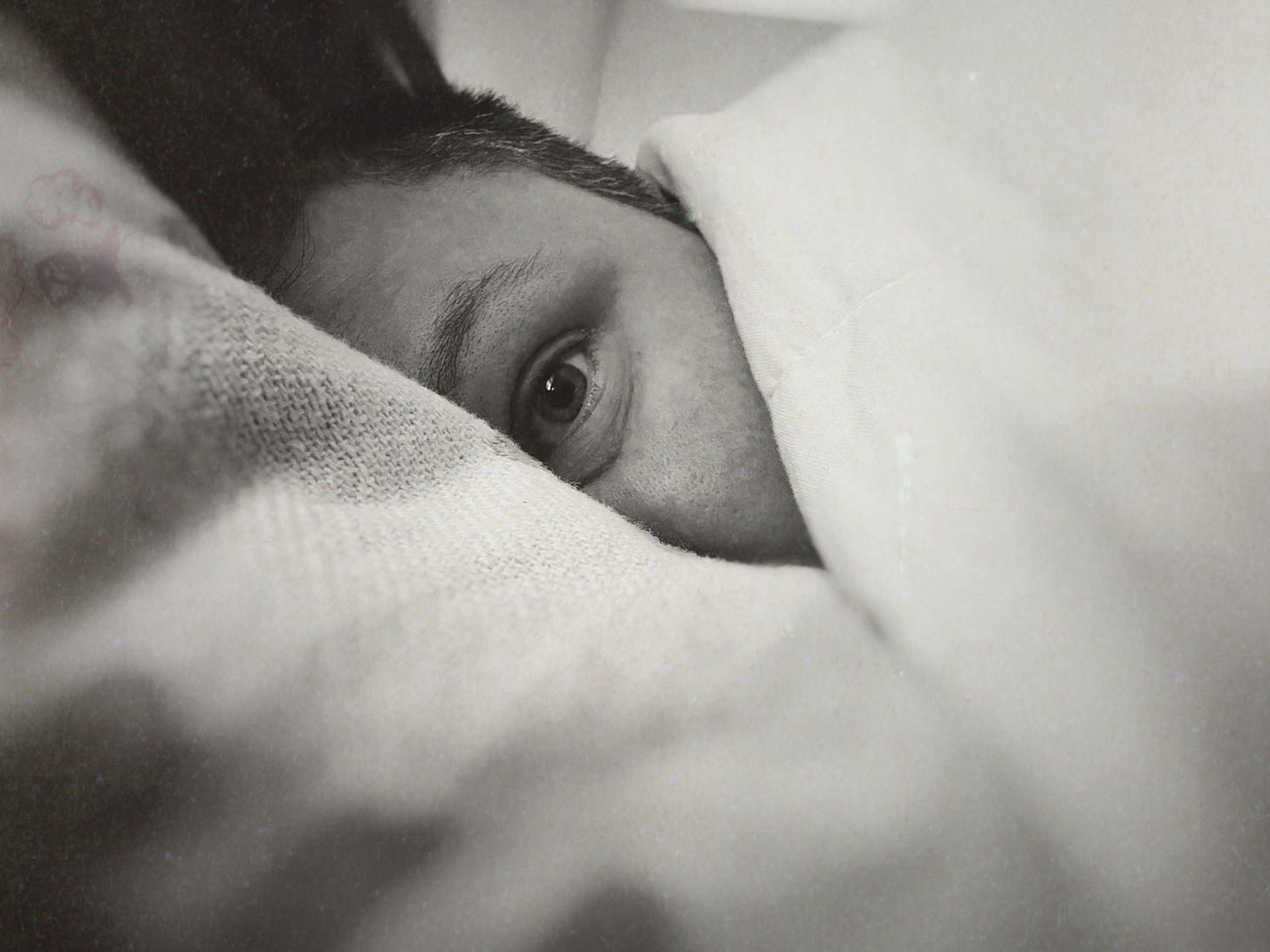 A woman in her 30. Black and white. She's wrapped in blankets so that only her one eye is showing. She's looking right at the camera.