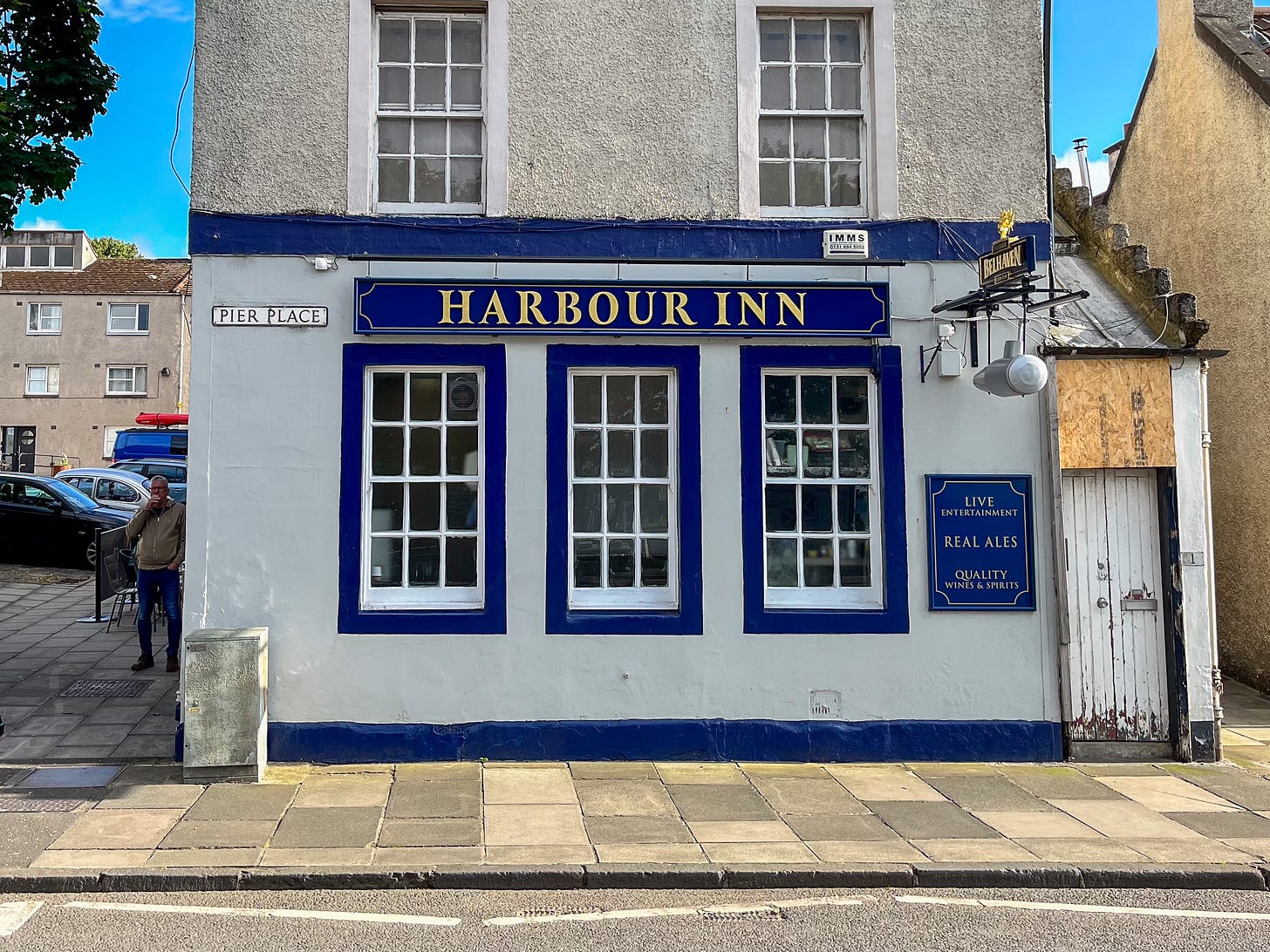 A white and blue outside of a pub on a sunny day. The Harbour iInn sign is in gold serif lettering.