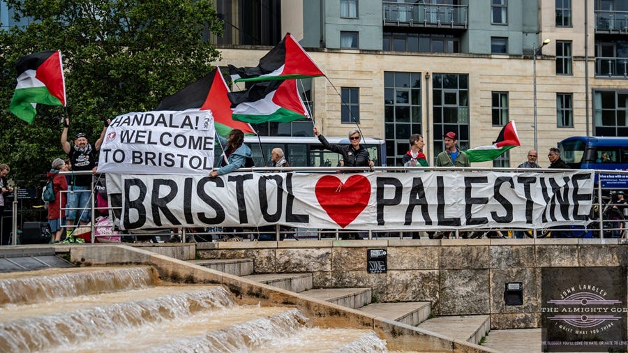 Pro-Palestinian protesters in Bristol holding a Bristol Loves Palestine banner and Palestinian flags at a demonstration in the city centre