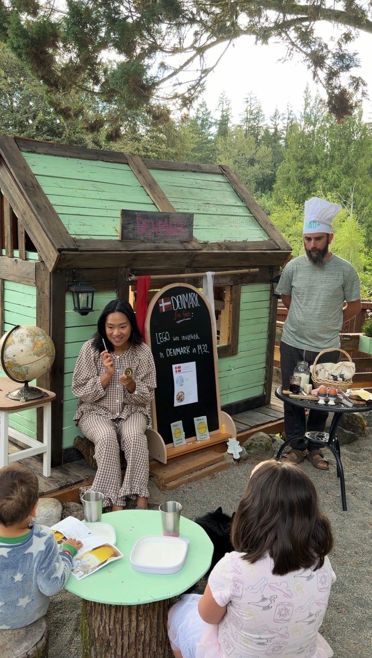 Woman leads an outdoor cooking activity for children while a chef prepares food nearby.