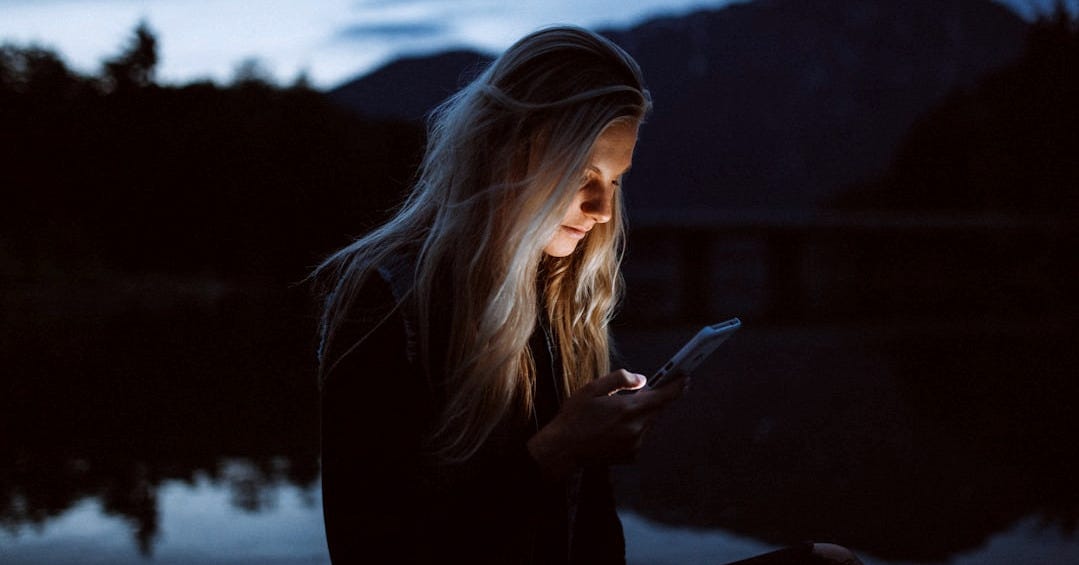 woman looking at phone beside body of water