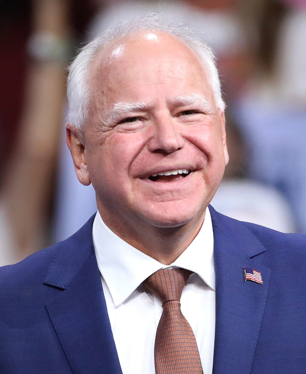 Walz headshot; smiling, wearing checked tie and blue suit; balding and grey hair