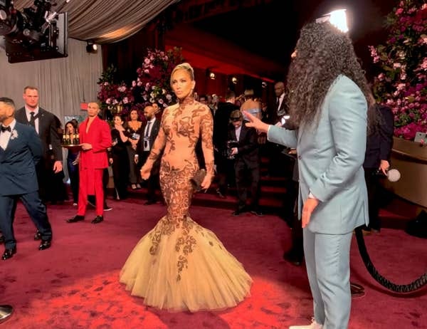 J.Lo posing for a camera while Cole speaks to her on the Globes carpet
