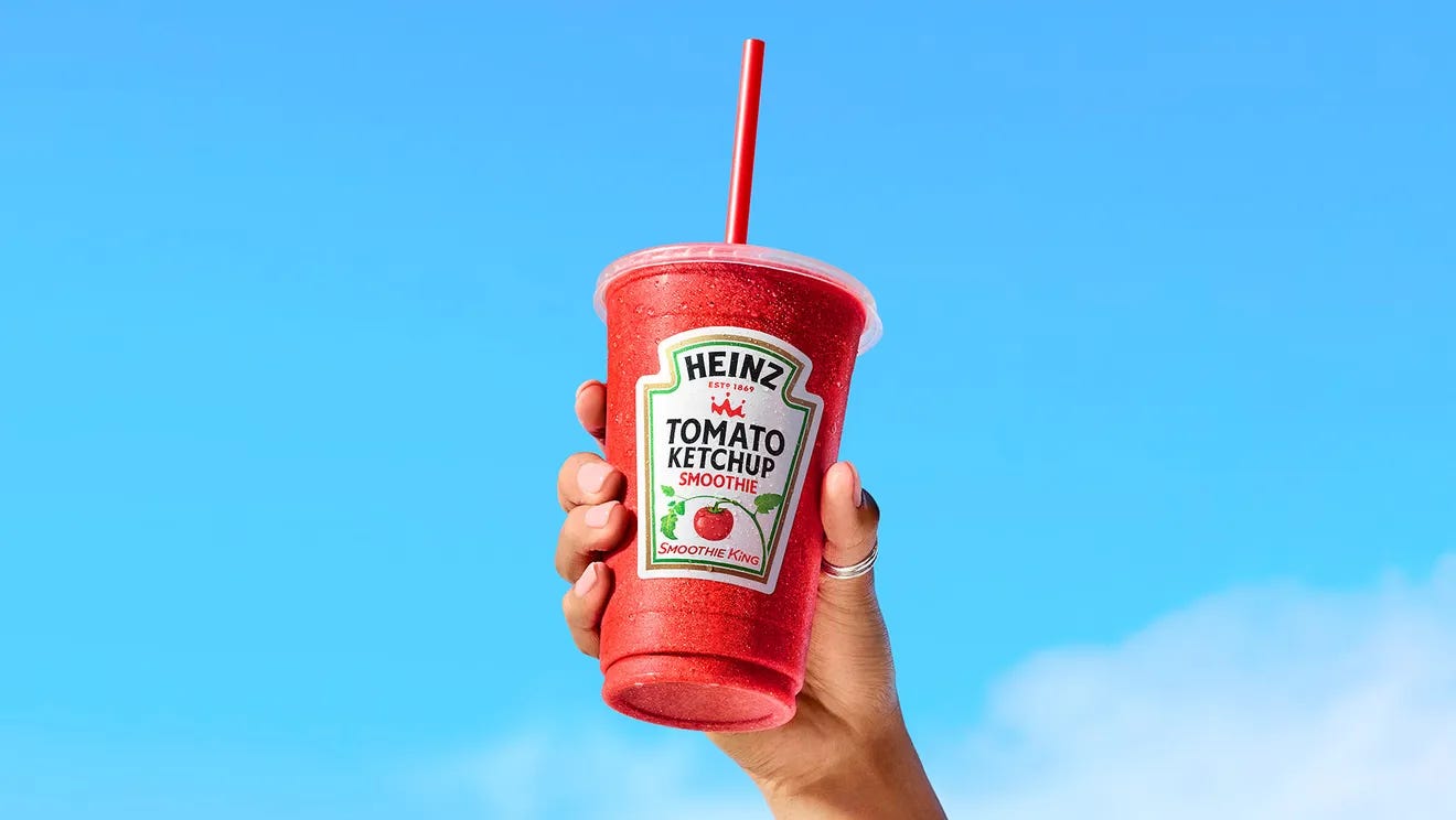 A plastic cup with a red drink inside and the Heinz ketchup label on the front