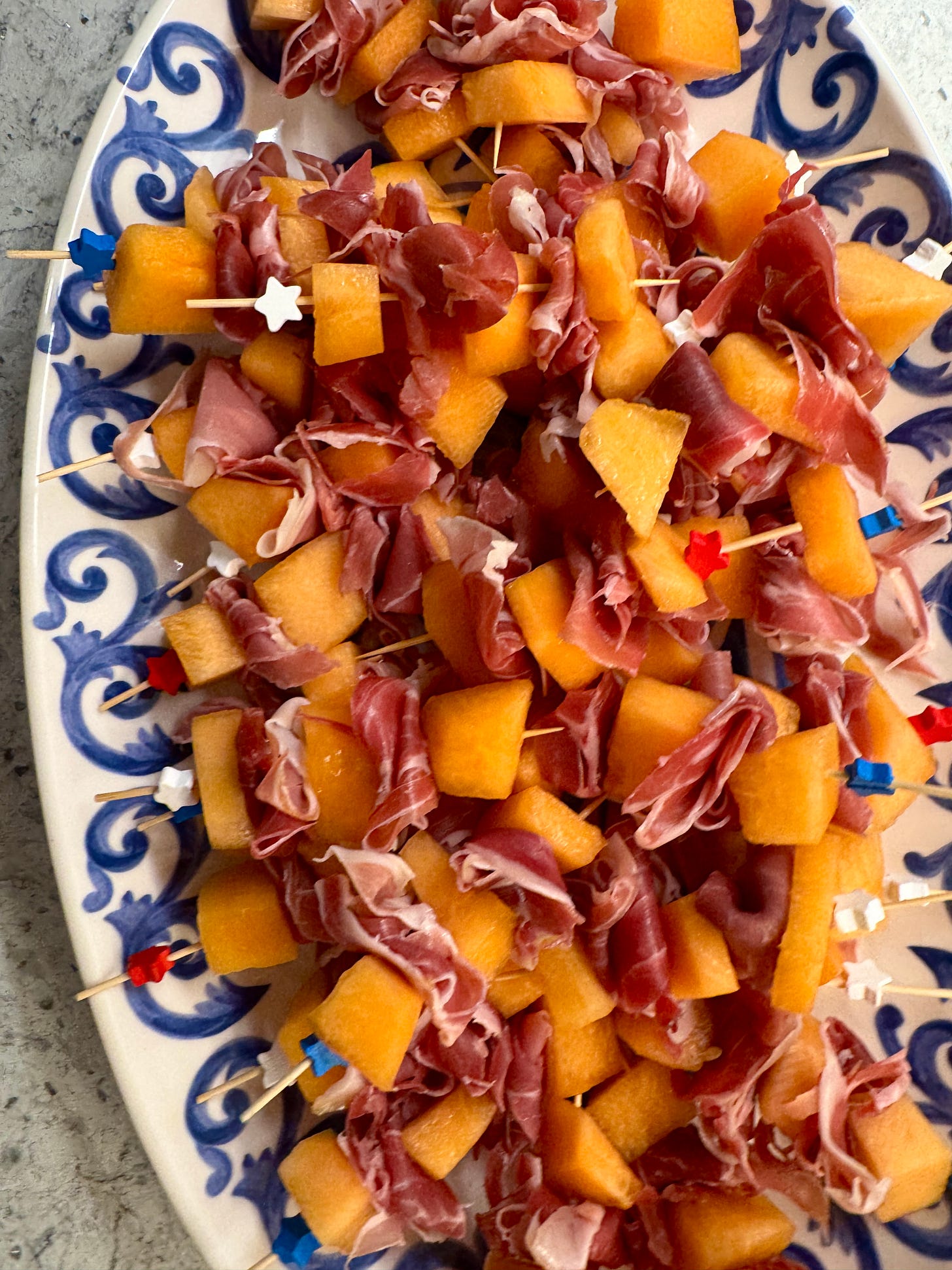 Salty prosciutto & fresh melon on simple skewers on a blue & white platter with red, white, and blue skewers