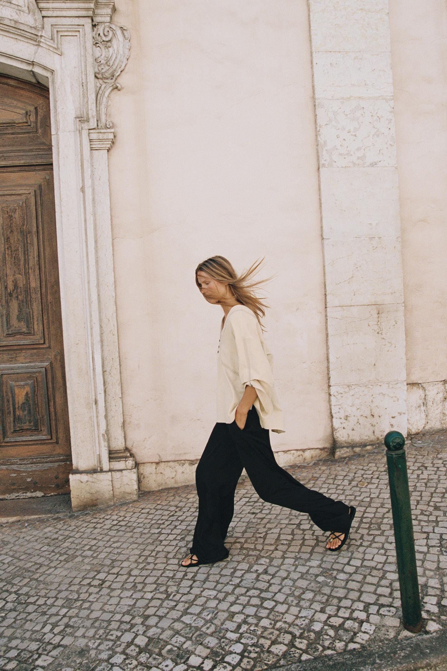 Outfit featuring a loose beige V-neck blouse with wide sleeves, flowing black trousers with side pockets, and black strappy sandals. Outfit featuring a loose beige V-neck blouse with wide sleeves, flowing black trousers with side pockets, and black strappy sandals.