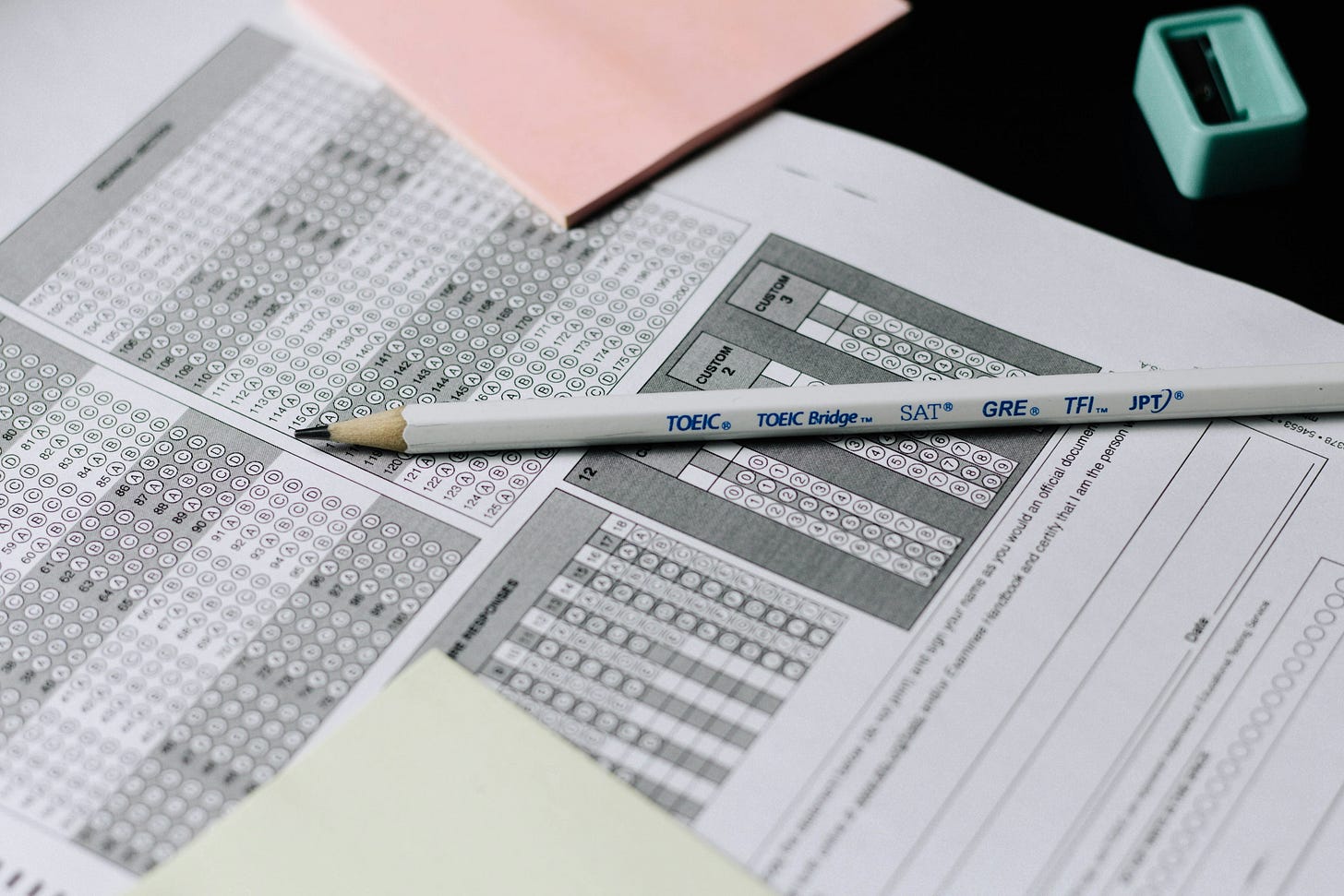 a pencil on top of a standardized test sheet with two sticky notes (pink and pale yellow) a pencil on top of a standardized test sheet with two sticky notes (pink and pale yellow)
